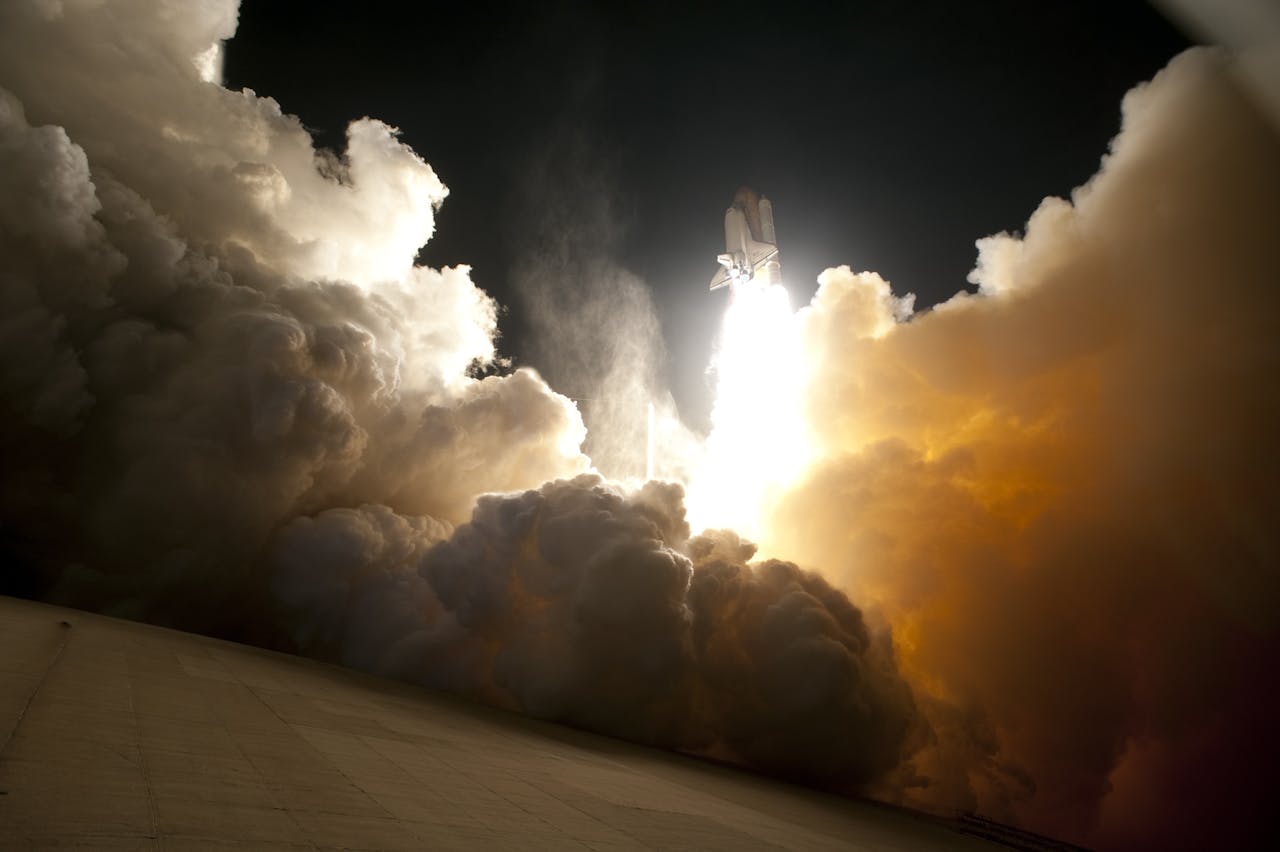 who-we-are A dramatic image of a space shuttle launching into the night sky, surrounded by billowing smoke and intense light.
